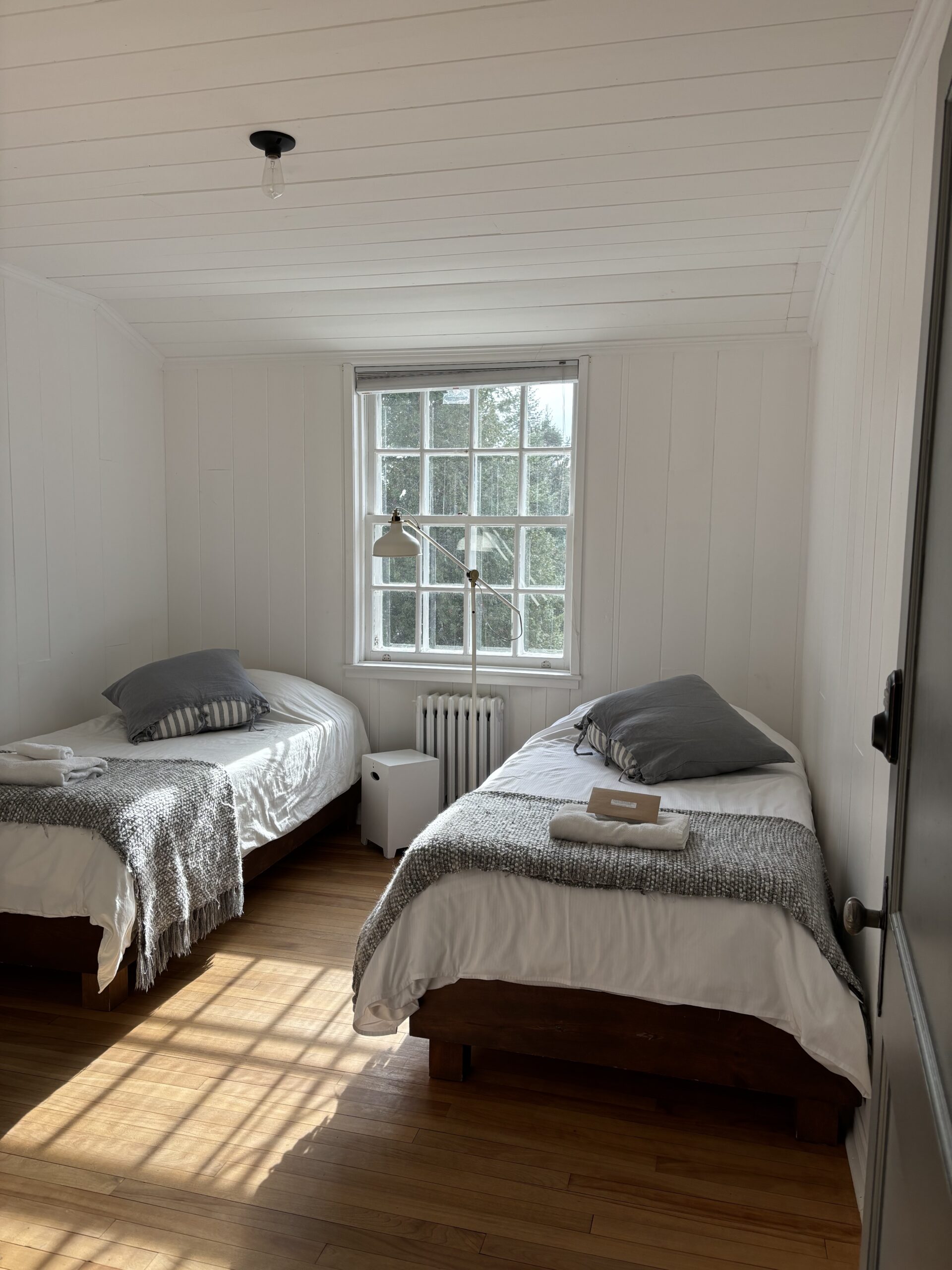 Chambre à occupation double avec deux lits simples, linge de lit gris et lumière naturelle au Havre du Rocher, Val-Morin.