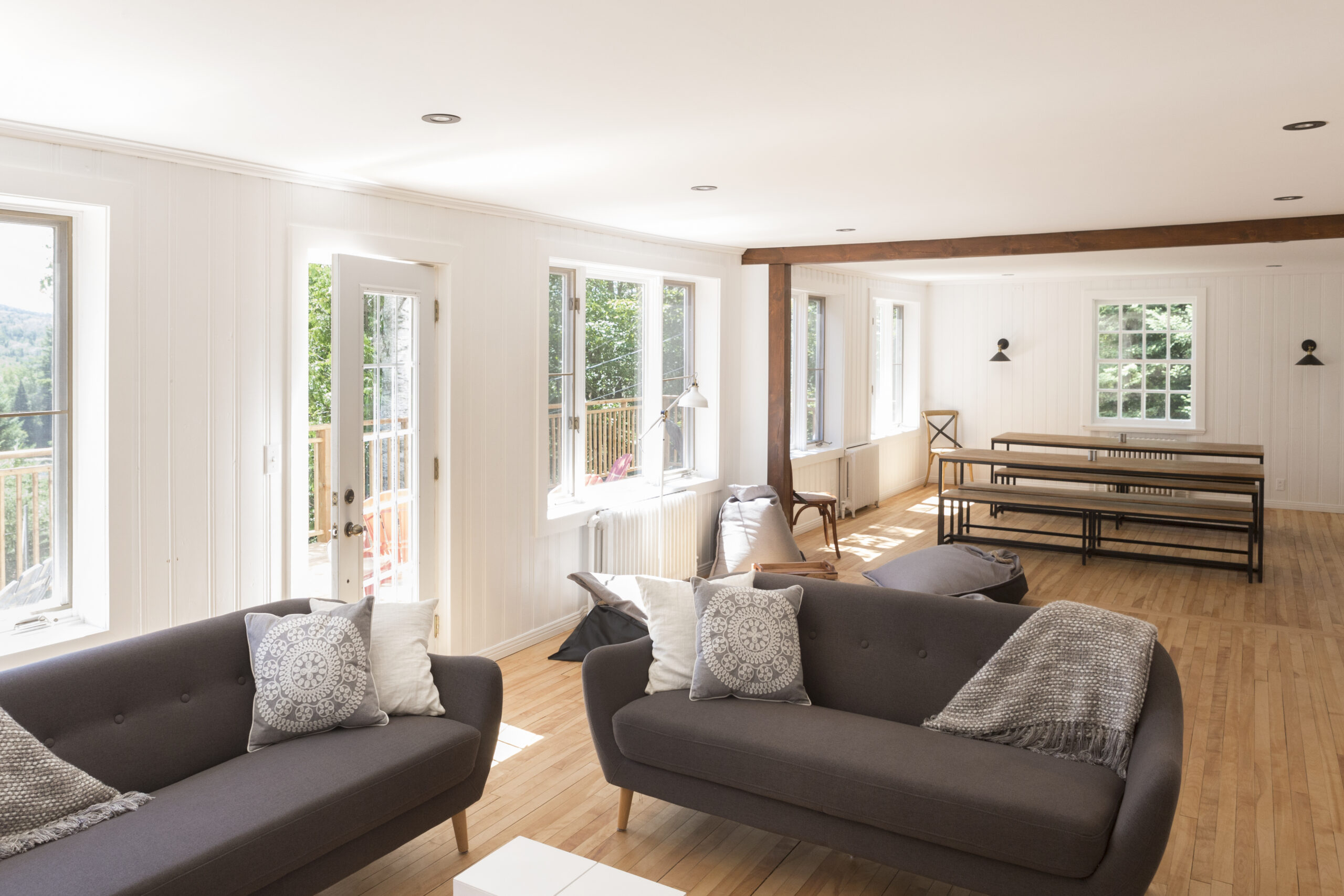 Salon lumineux avec canapés confortables, coussins décoratifs et grandes fenêtres donnant sur la nature au Havre du Rocher, Val-Morin.