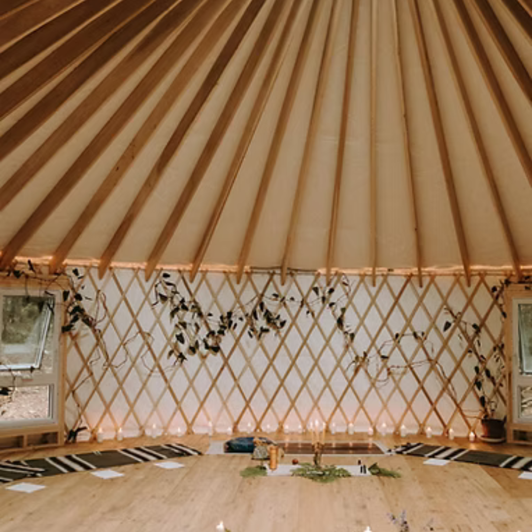 Intérieur de yourte décorée avec tapis, bougies et feuillage, prête pour une séance de méditation ou un cercle de partage.