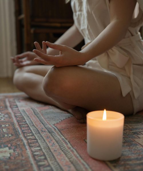 Personne assise en posture de méditation avec une bougie allumée sur un tapis aux motifs orientaux.