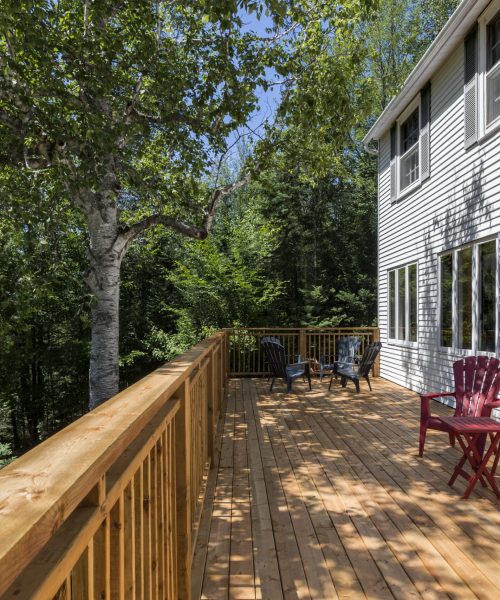 Terrasse en bois avec chaises Adirondack rouges et noires, entourée d’arbres au Havre du Rocher, Val-Morin.