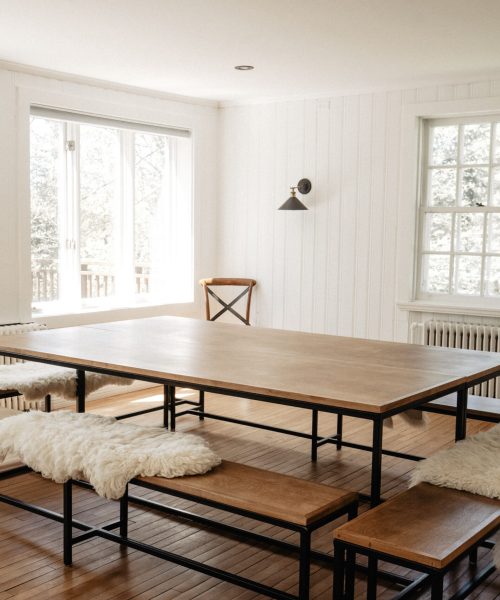 Salle à manger lumineuse avec grande table en bois et bancs recouverts de fourrures au Havre du Rocher, Val-Morin.